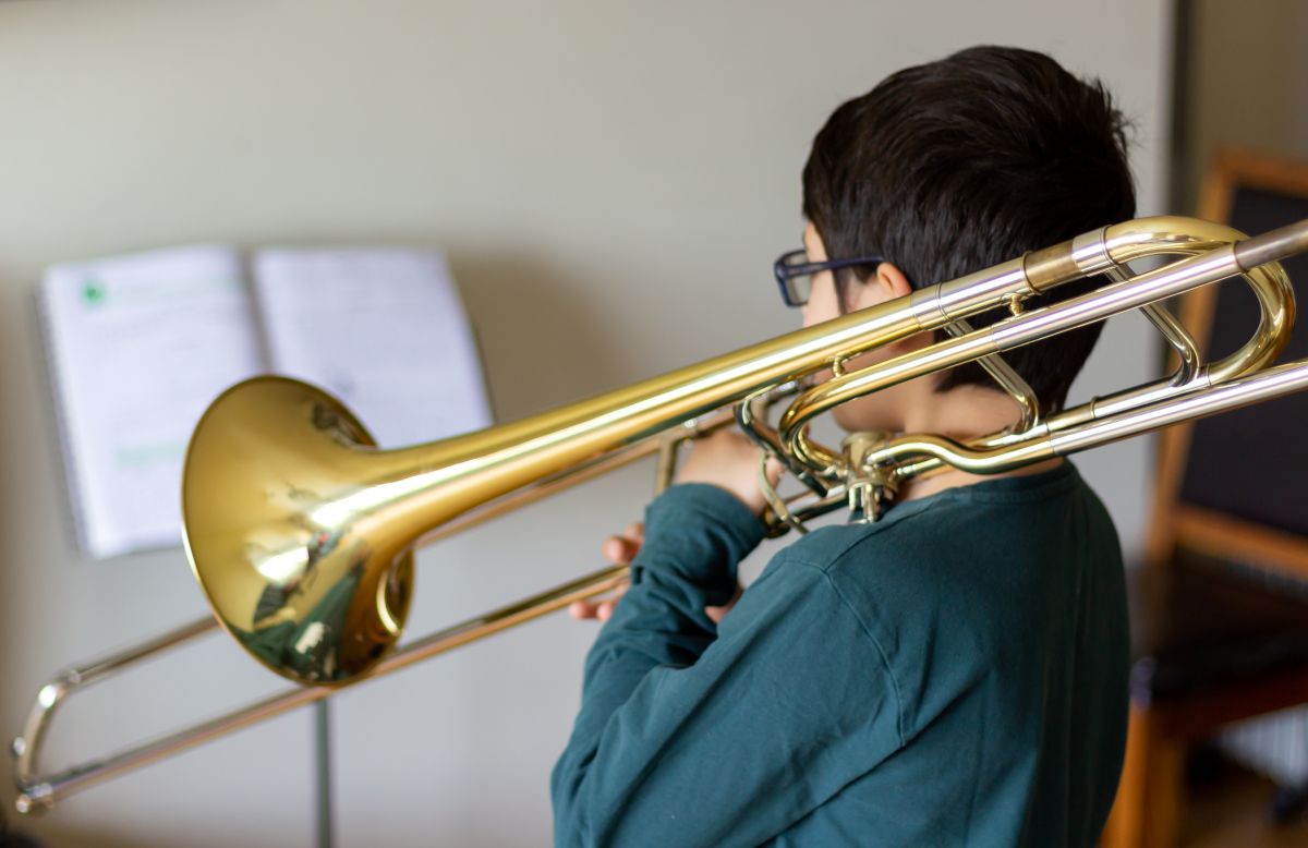A child reading sheet music while playing the trombone at home